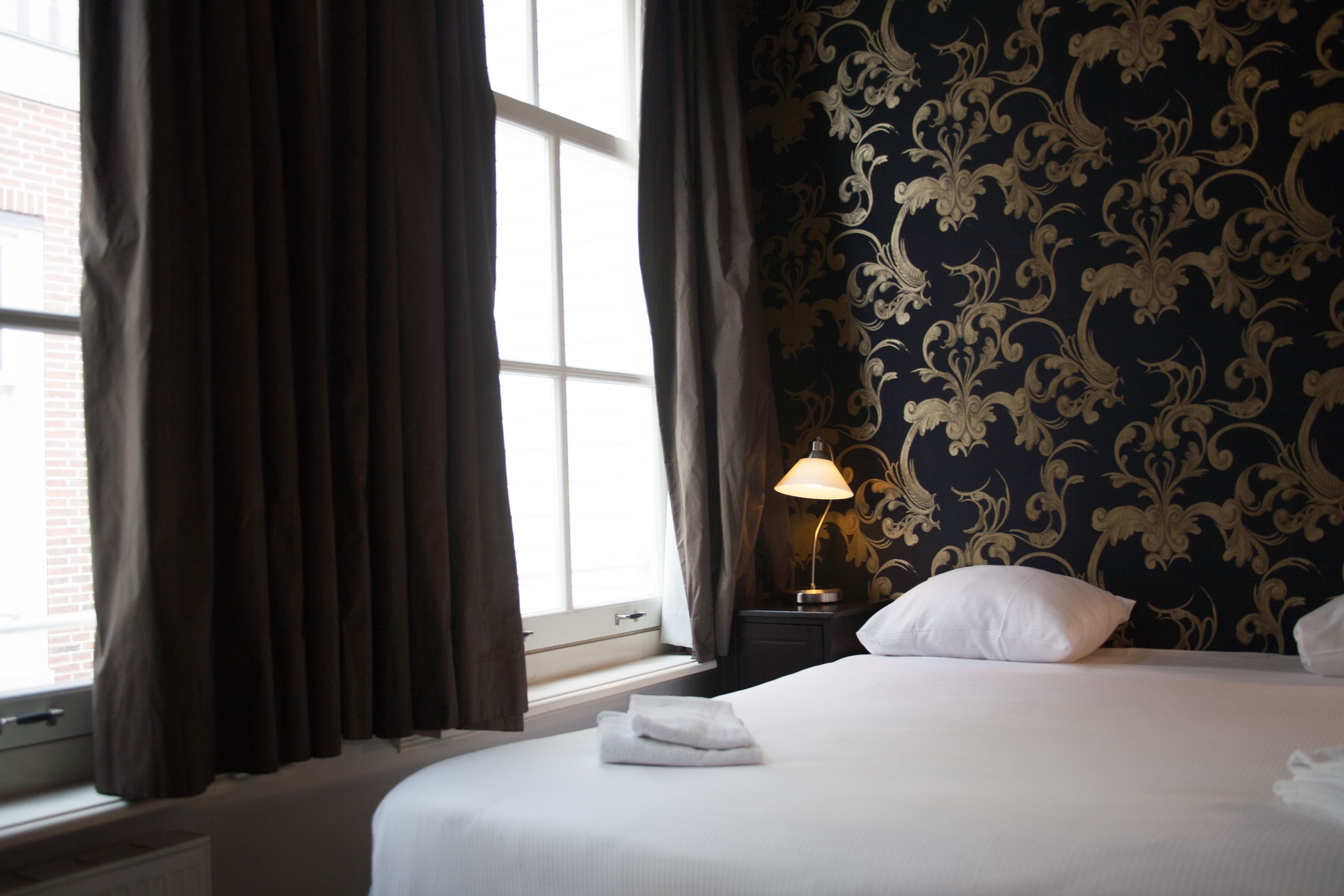 Une chambre d’hôtel avec un lit, une table de chevet, une lampe et une fenêtre avec des rideaux.