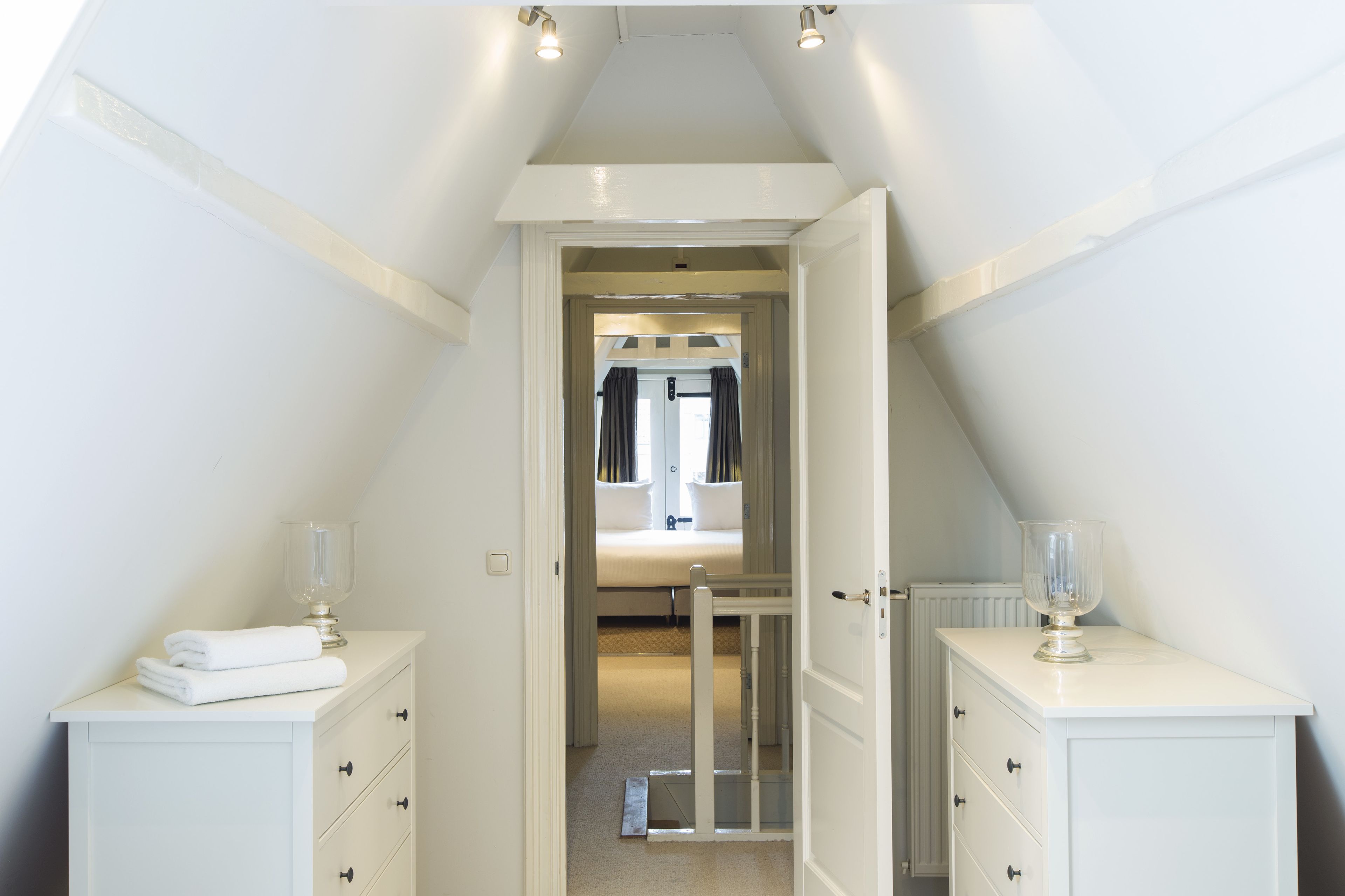 A narrow hallway leading to a bedroom with a bed, a radiator, and a glass door.