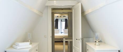 A narrow hallway leading to a bedroom with a bed, a radiator, and a glass door.