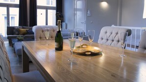 Una sala moderna con una mesa de centro de madera, una botella de champán y varios vasos. Se ve un sofá y un sillón con cojines al fondo.