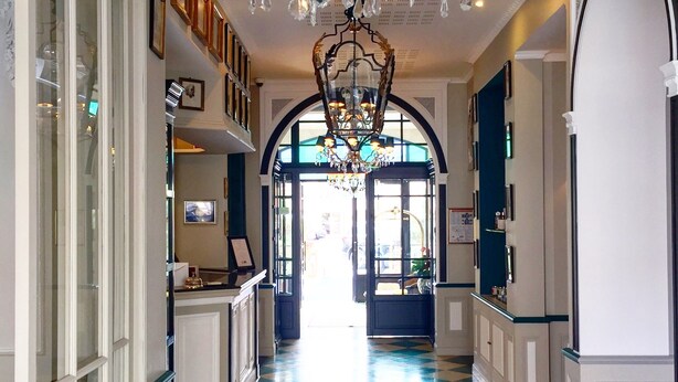 Um corredor com piso xadrez, um candelabro e quadros nas paredes.