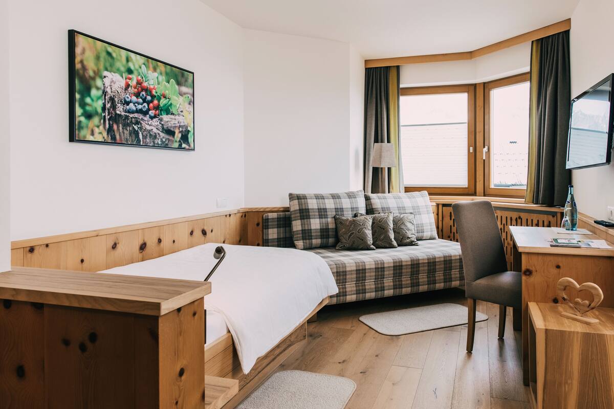 Una habitación acogedora con cama, sofá, escritorio y ventana con cortinas.