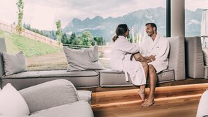 A couple in white robes sitting on a grey sofa with a mountain view.