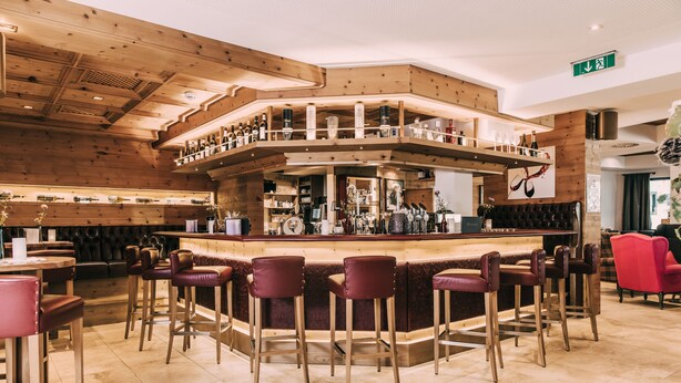 A bar area with wooden paneling, multiple bar stools, and a variety of bottles and glasses on shelves.