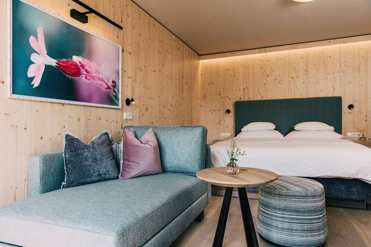 Una habitación de hotel moderna con sofá, reposapiés y una cama con cabecera verde.