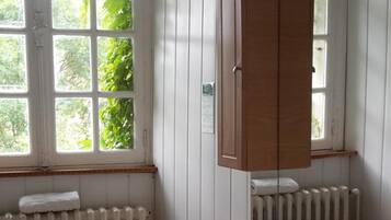 Une salle de bain avec un meuble-lavabo en bois, un lavabo blanc et un miroir. Une fenêtre offre une vue sur la verdure à l’extérieur.