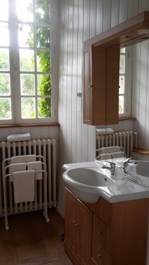 A bathroom with a wooden vanity, a white sink, and a mirror. There is a window with a view of greenery outside. - Hotel du Golf de Clécy (Clecy)