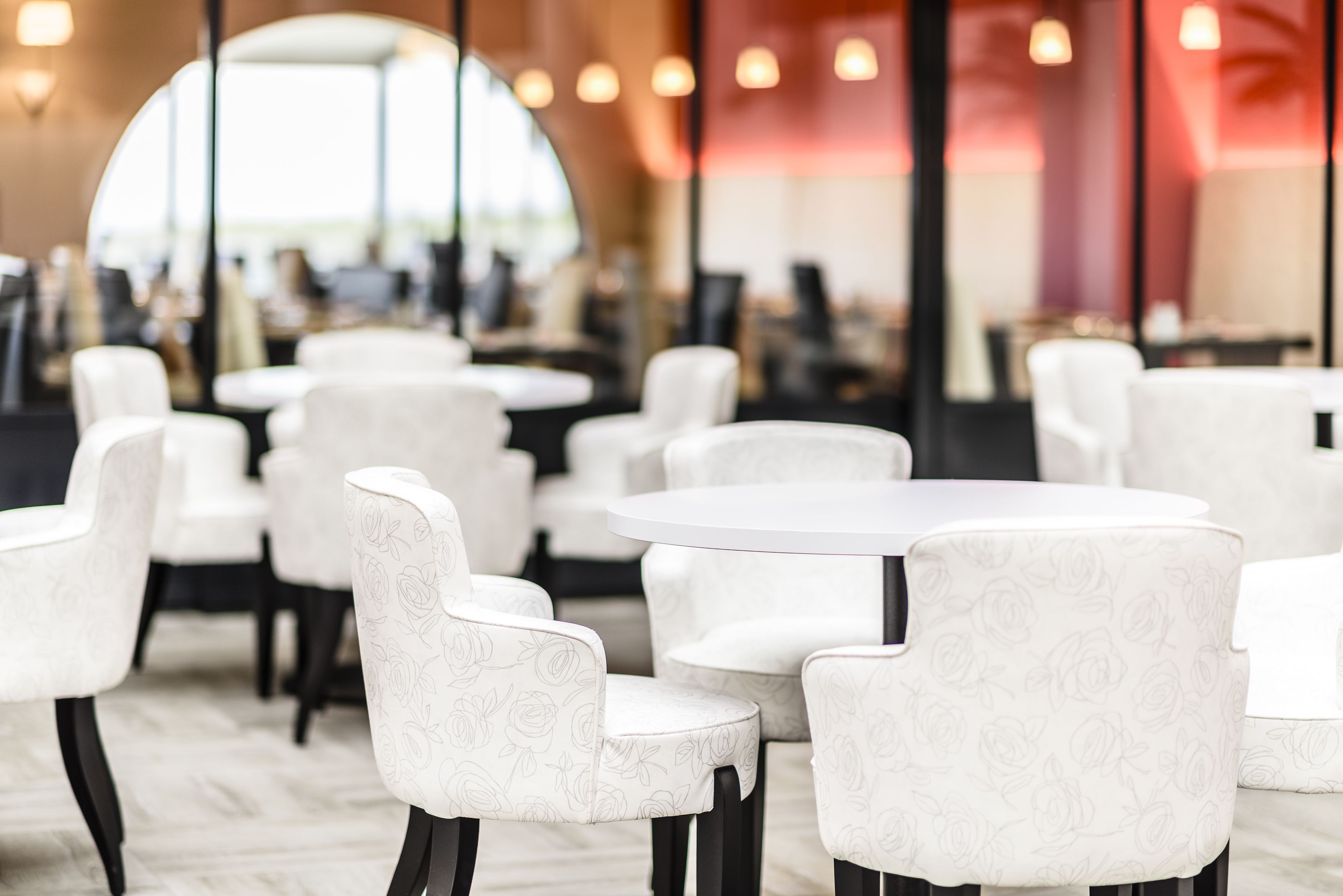 A modern restaurant interior with white floral-patterned chairs and round tables.