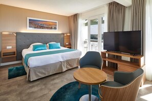 A hotel room with a large bed, a TV, a small table, and a balcony with a view.