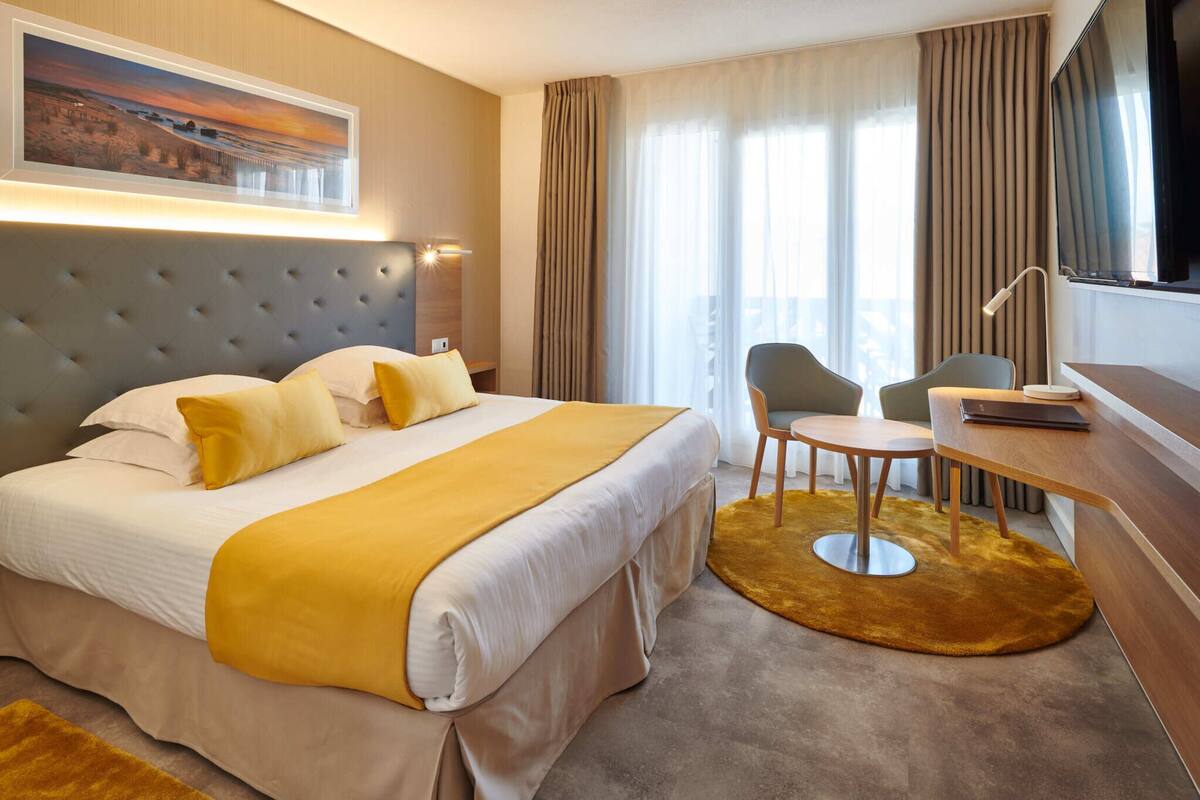A hotel room with a large bed, a desk, a chair, a television, and a painting on the wall.