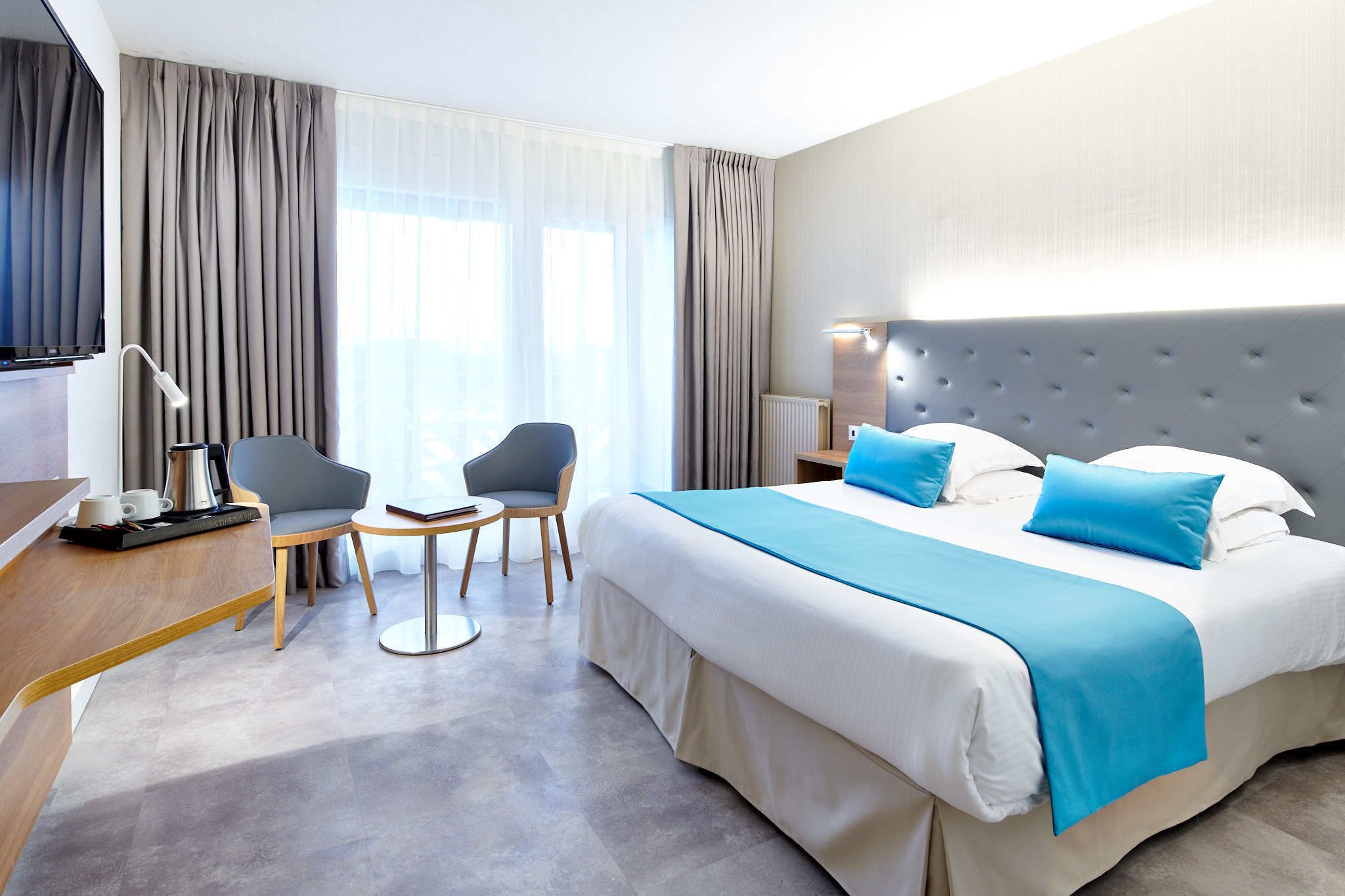 A hotel room with a large bed, a desk with a coffee maker, a chair, and a small table.