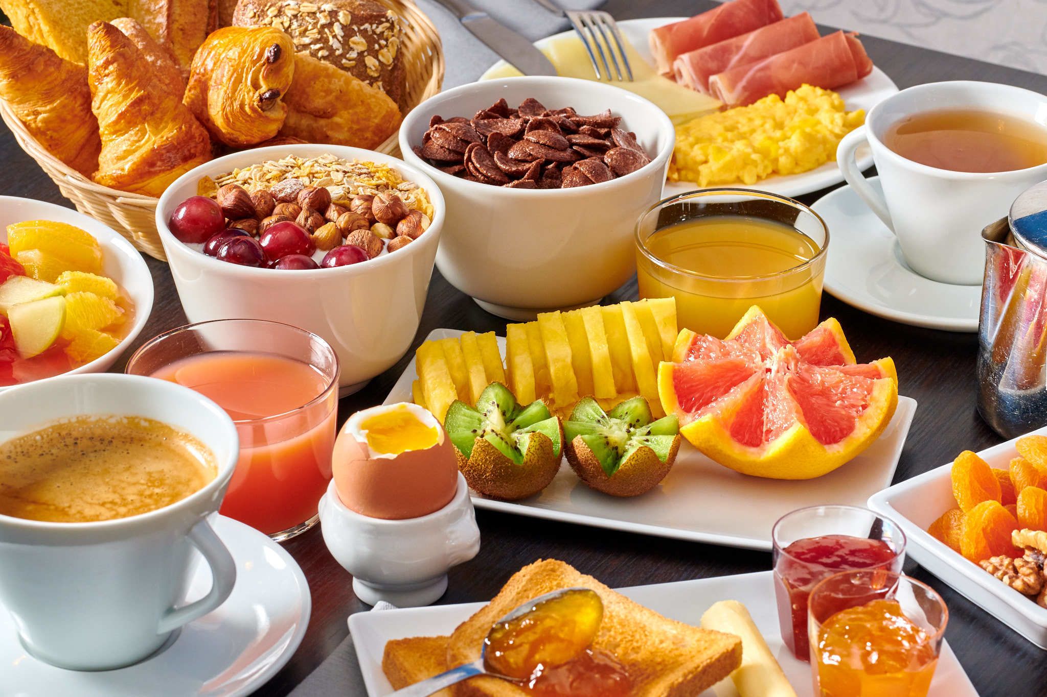 A breakfast spread with croissants, fruits, eggs, and beverages.
