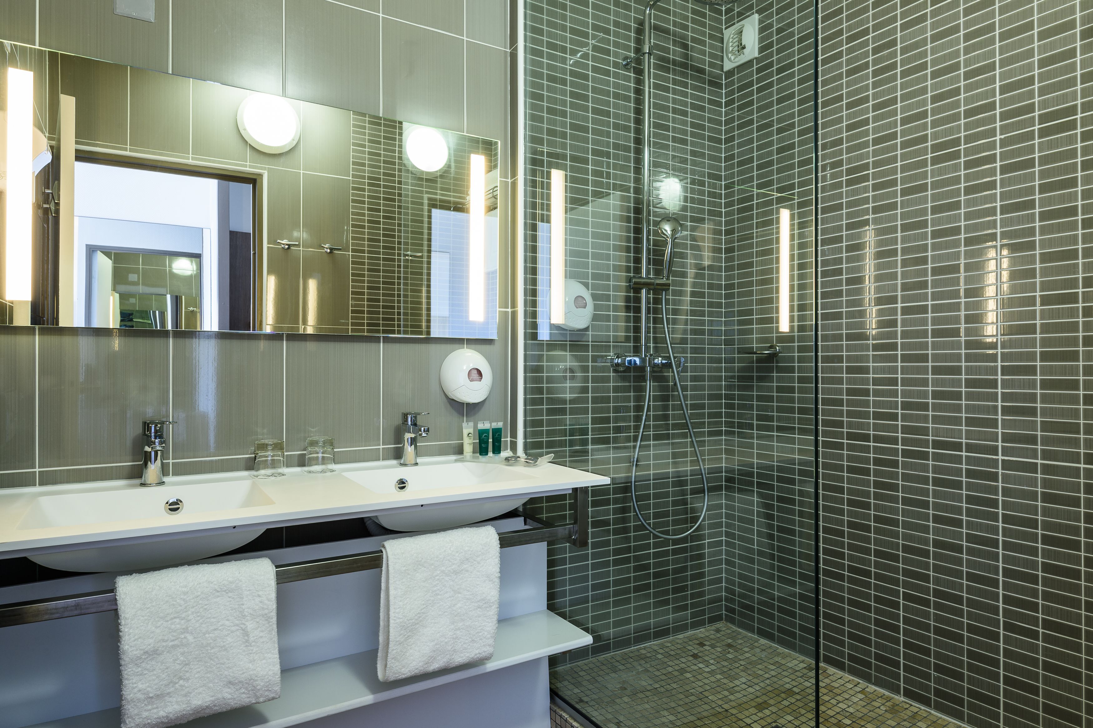 Un baño moderno con un espejo grande, dos lavamanos, una ducha y un perchero para toallas.