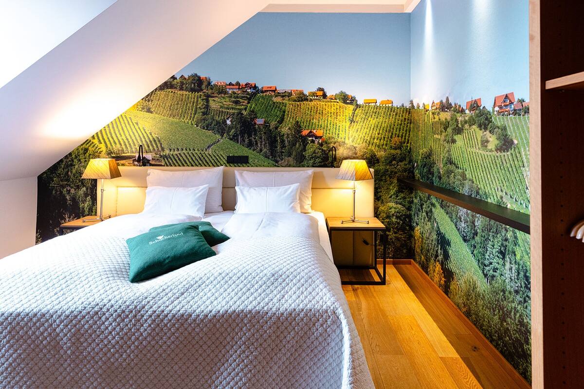 A bedroom with a large bed, two bedside tables, and a mural of a vineyard on the wall.