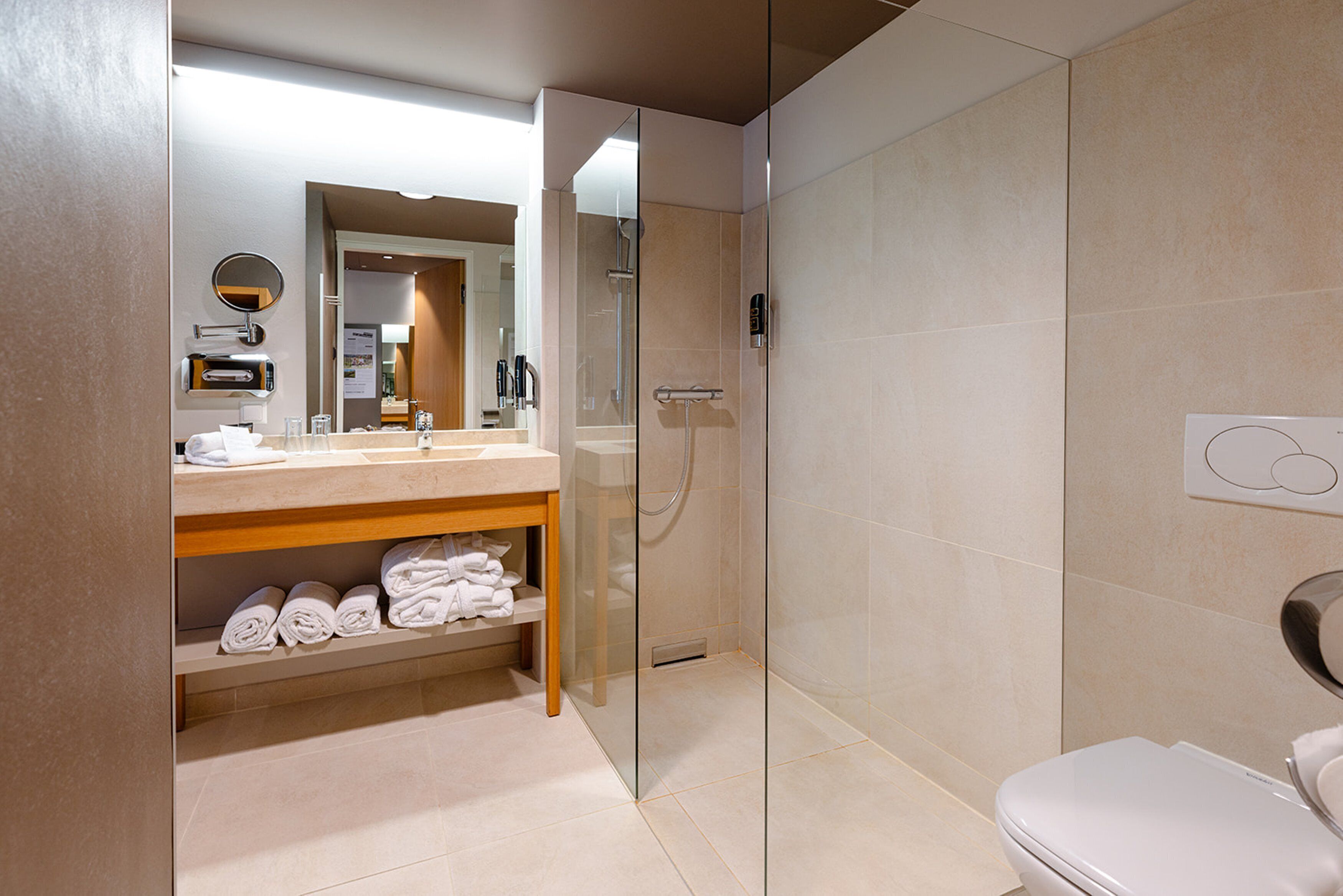 Ein modernes Badezimmer mit einer gläsernen Duschkabine, einer weißen Toilette und einem Waschtisch mit Spiegel und Handtuchhalter.