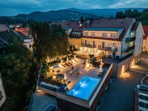A rooftop pool area with lounge chairs and umbrellas, surrounded by buildings and trees. - Hotel Stainzerhof (Stainz)