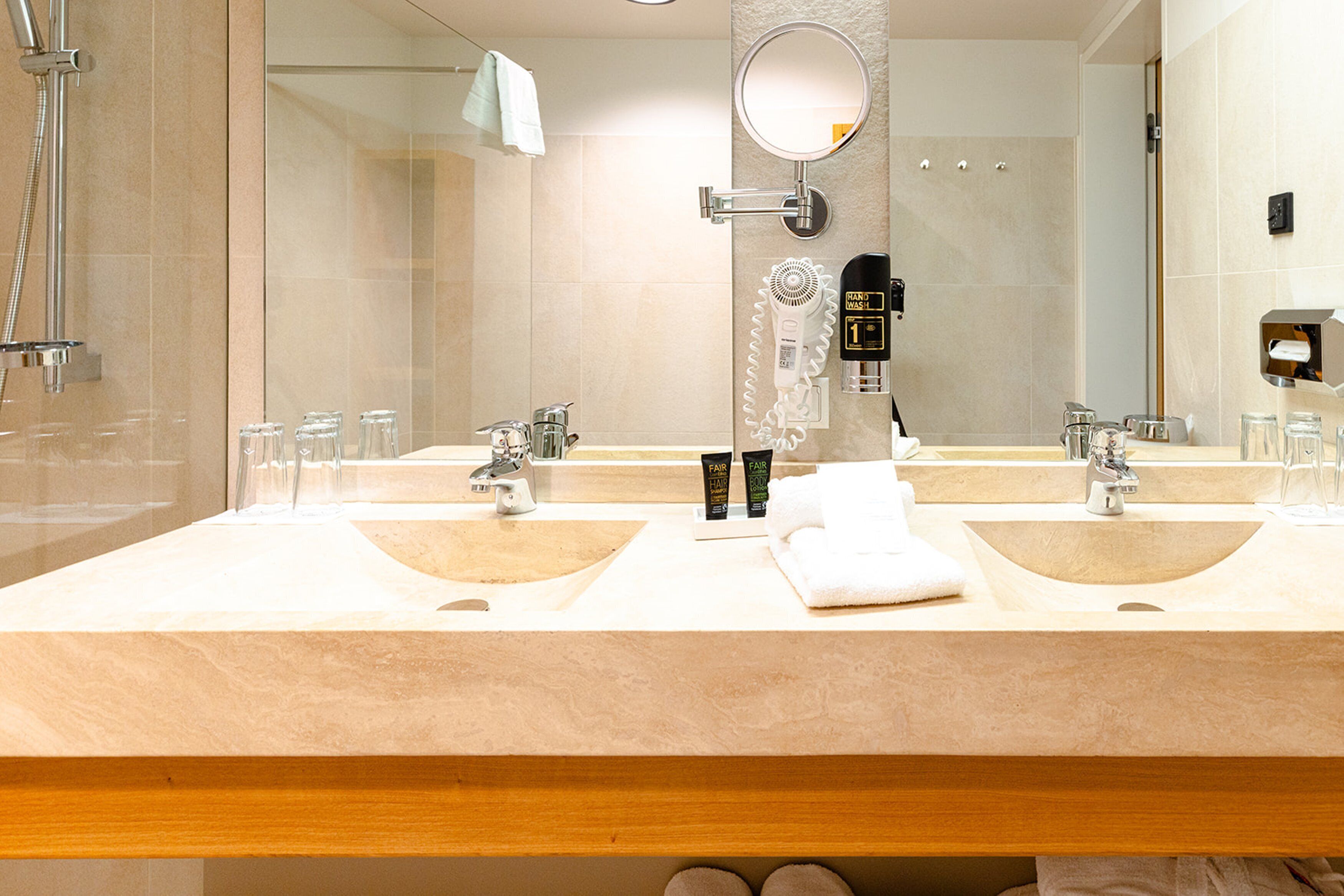 A modern bathroom with two sinks, a large mirror, and a hairdryer.