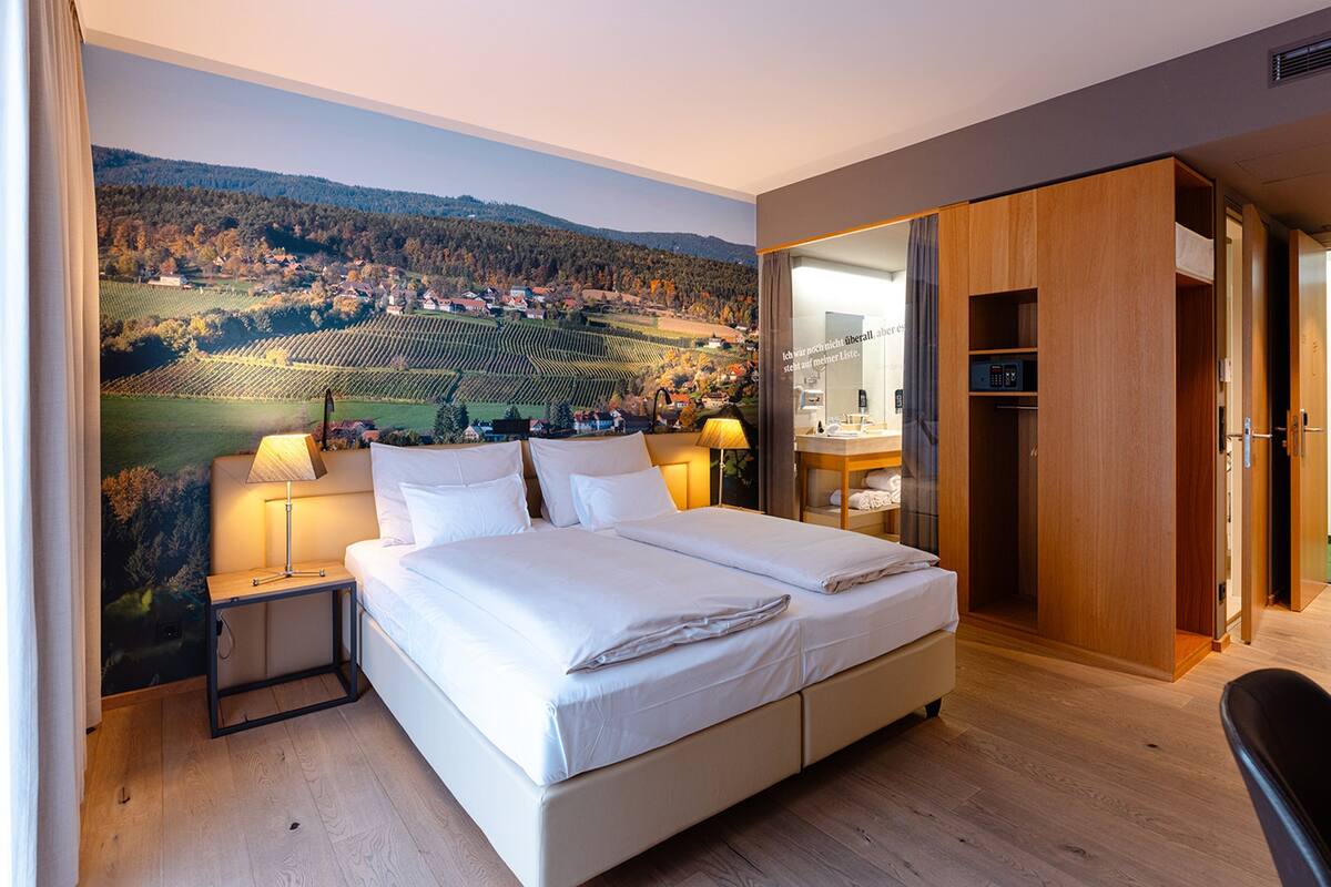 A bedroom with a large bed, bedside lamps, a wooden wardrobe, and a mural of a vineyard on the wall.