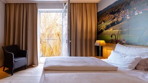 Habitación de hotel con una cama grande, una silla, una lámpara y vistas a un viñedo por la ventana.