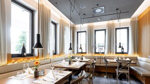 Un restaurante con varias mesas, sillas y un amplio ventanal con cortinas.