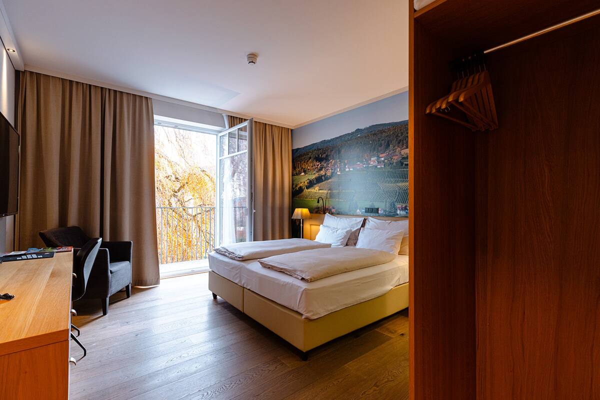 A hotel room with a bed, a desk, a chair, and a large window with curtains.