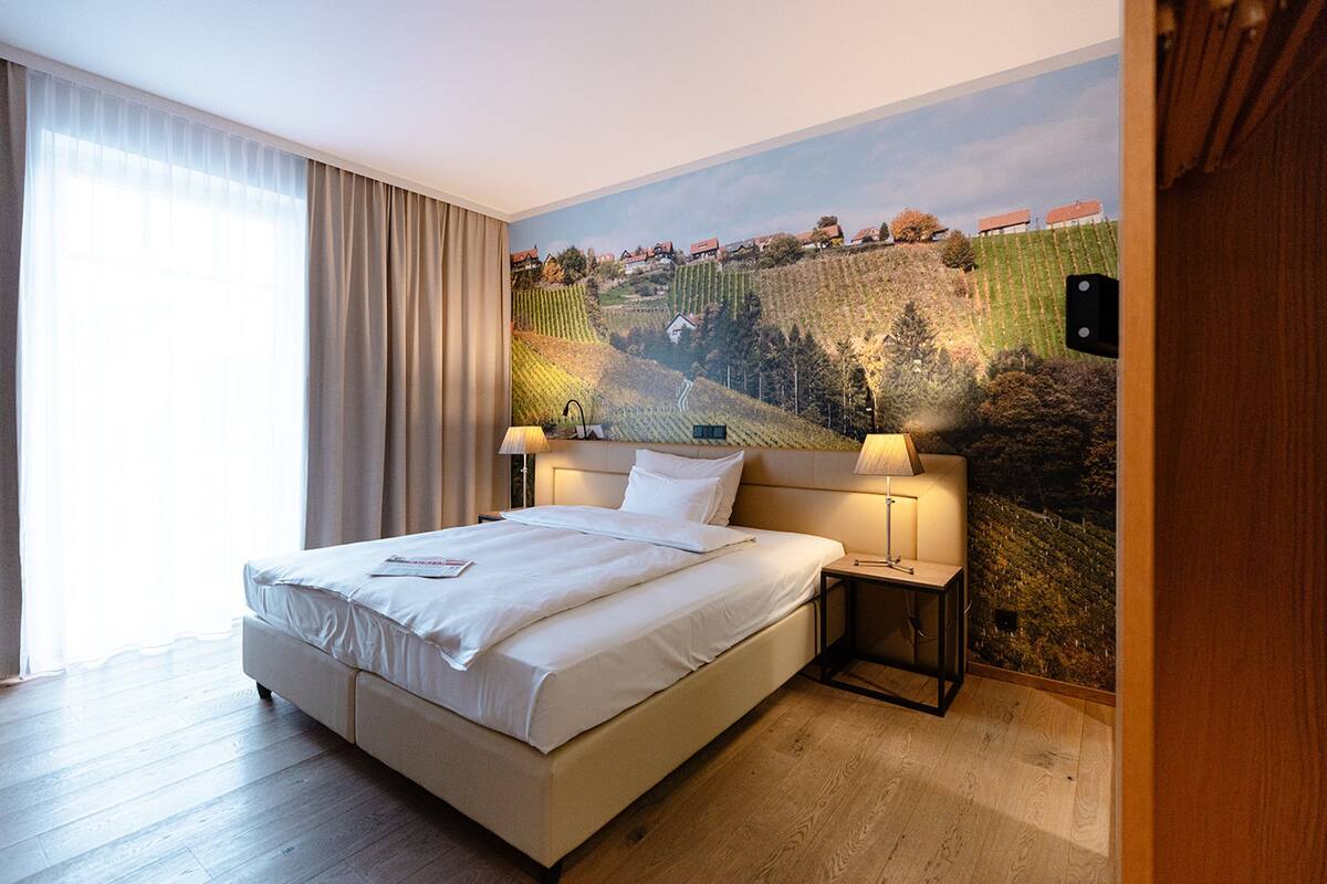 A hotel room with a large bed, two bedside tables, and a mural of a vineyard on the wall.