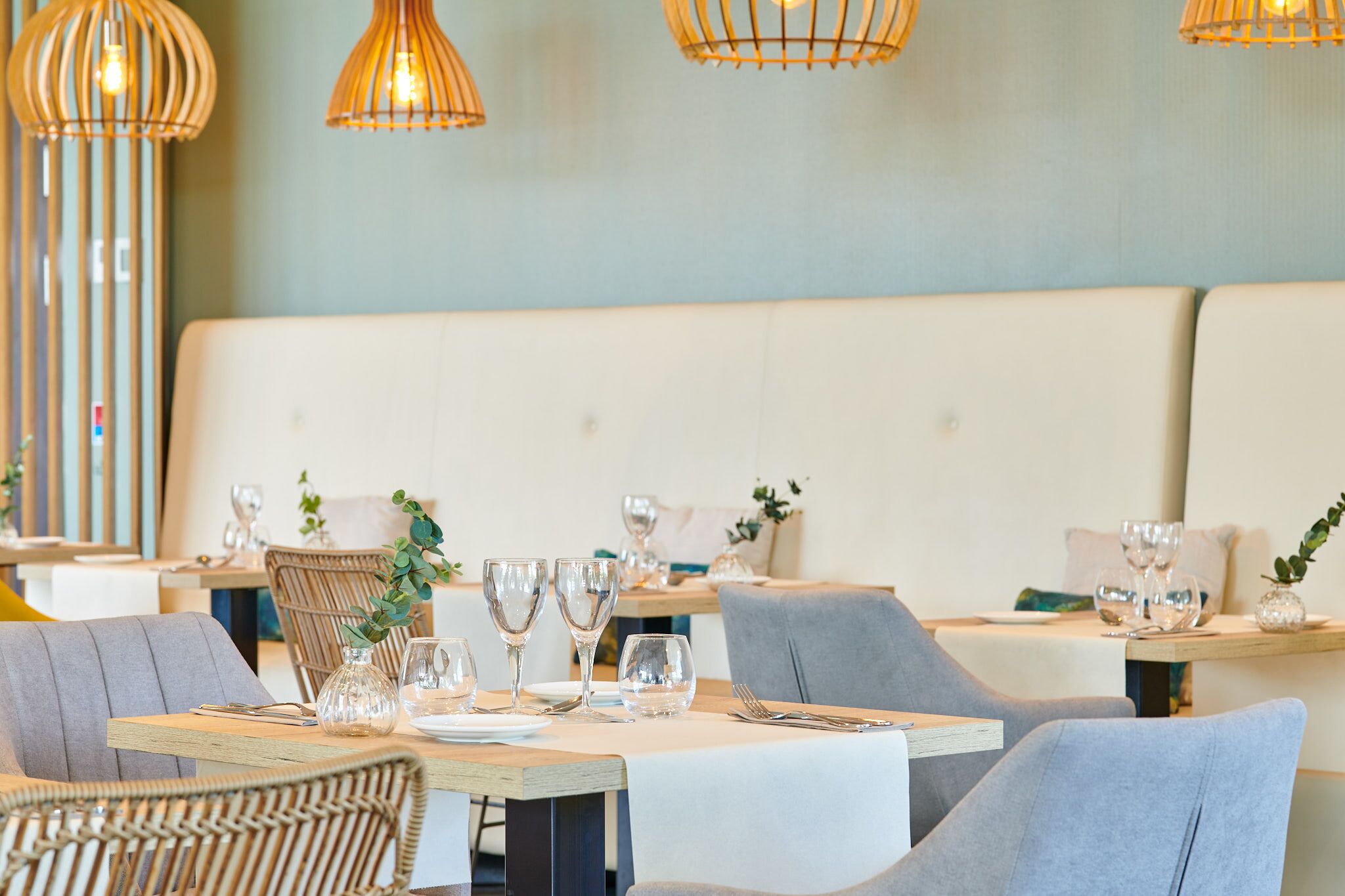 Un restaurante con una larga mesa de madera preparada para comer, rodeado de sillas de mimbre y un banco acolchado.