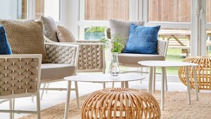A modern outdoor seating area with wicker furniture, a round table, and a vase with greenery. - Hôtel Les Terrasses d'Atlanthal (Anglet)