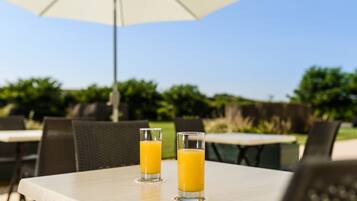 Two glasses of orange juice on a table under an umbrella.