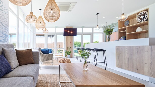 A modern living room with a sofa, coffee table, and wicker pendant lights. - Hôtel Les Terrasses d'Atlanthal (Anglet)