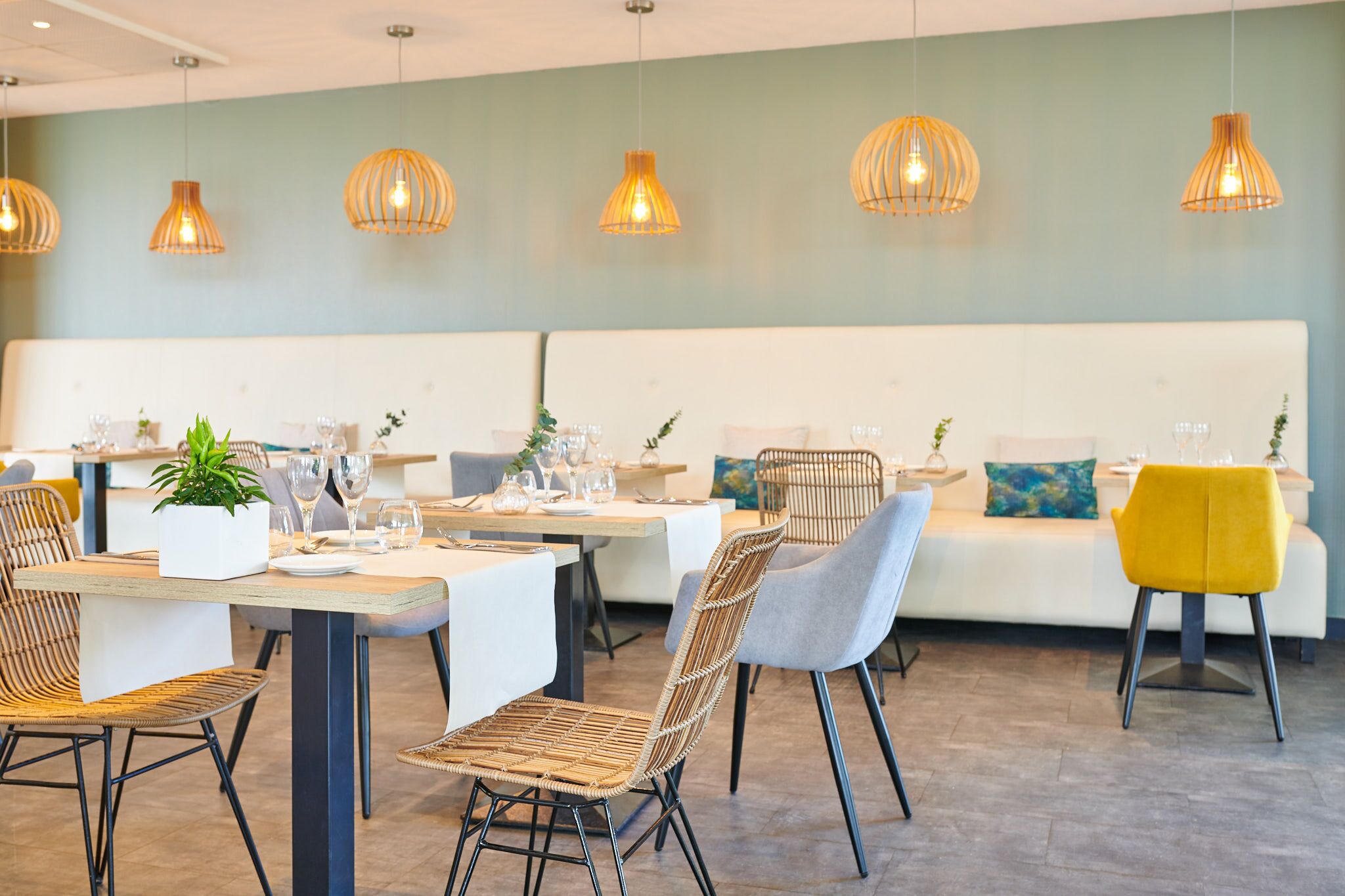 Ein Restaurant mit einer weißen Couch, Korbstühlen und hängenden Pendelleuchten.
