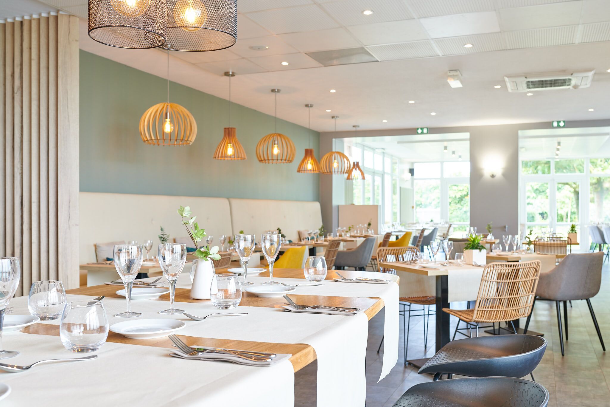 A restaurant with multiple tables set for dining, featuring a modern interior with pendant lighting and a view of the outdoors.