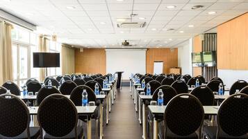 A conference room with rows of tables and chairs, a projector, and a screen.