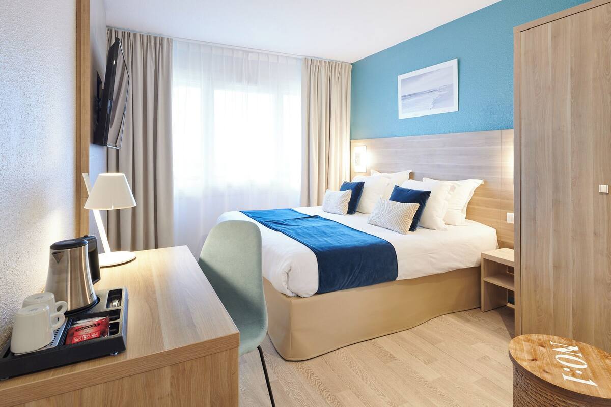 A hotel room with a bed, bedside tables, a lamp, a coffee maker, and a view of the outdoors.