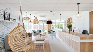 A modern reception area with a wooden reception desk, hanging rattan chairs, and a large window providing natural light. - Hôtel Les Terrasses d'Atlanthal (Anglet)