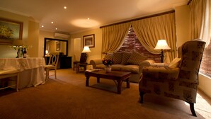 A well-lit living room with a sofa, armchair, coffee table, and a dining area with a table and chairs. - Little Tuscany Boutique Hotel (Sandton)