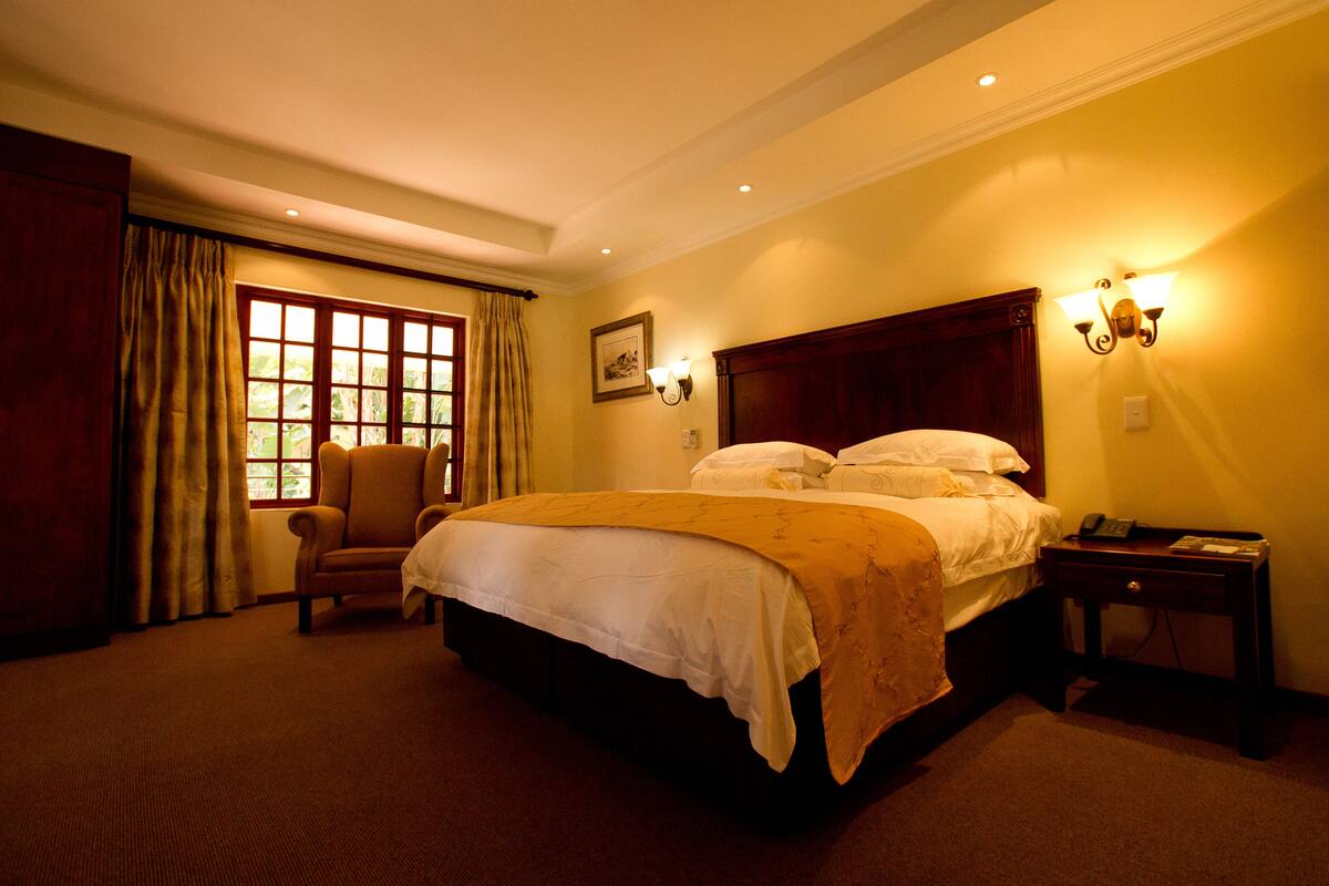 Une chambre d’hôtel avec un grand lit, une chaise, une table de chevet et une fenêtre avec des rideaux.