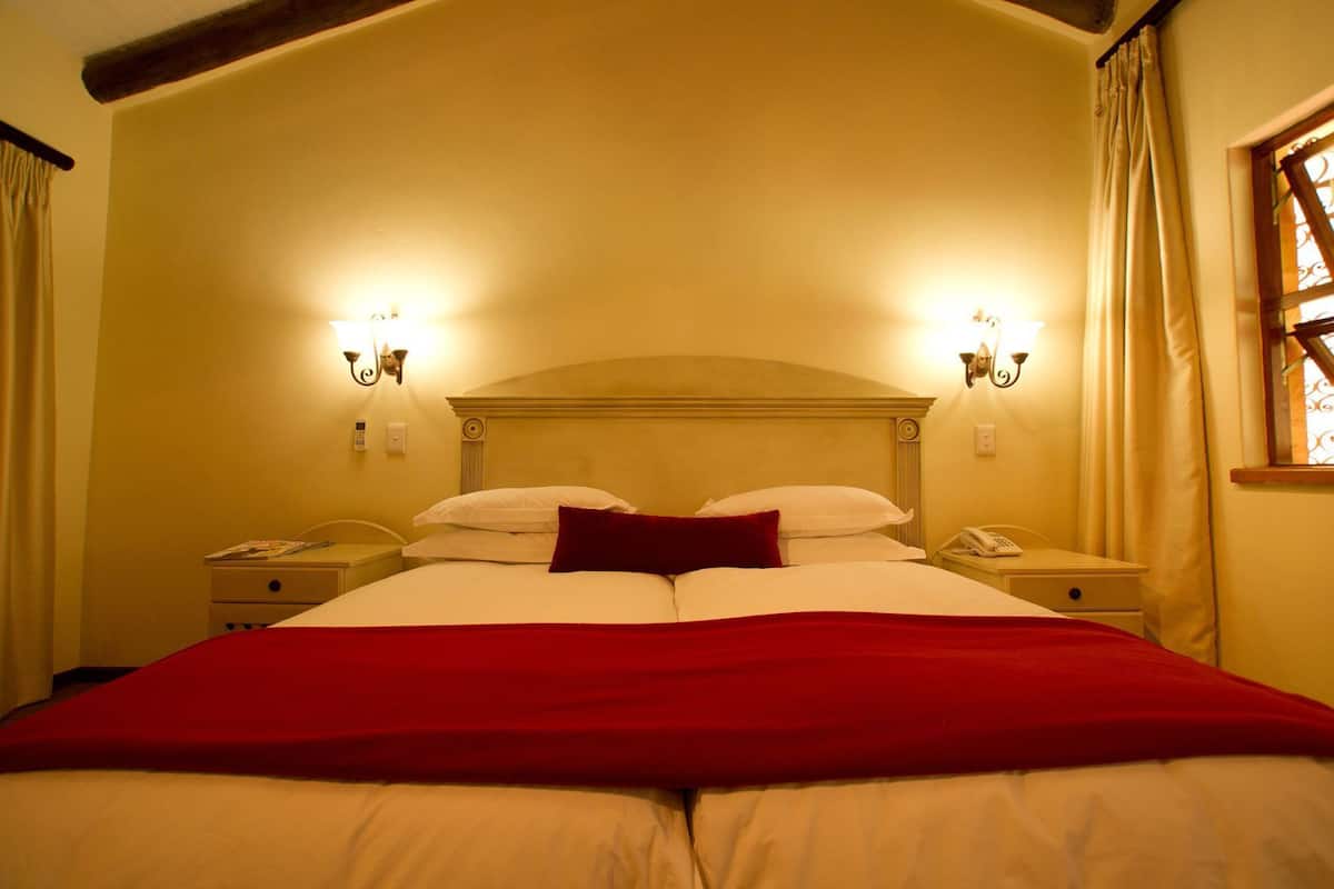 Une chambre d’hôtel avec un grand lit, deux tables de chevet, une tête de lit en bois et deux lampes fixées au mur.