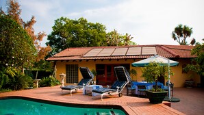 A pool area with lounge chairs and a table, surrounded by greenery and a building with a tiled roof. - Little Tuscany Boutique Hotel (Sandton)