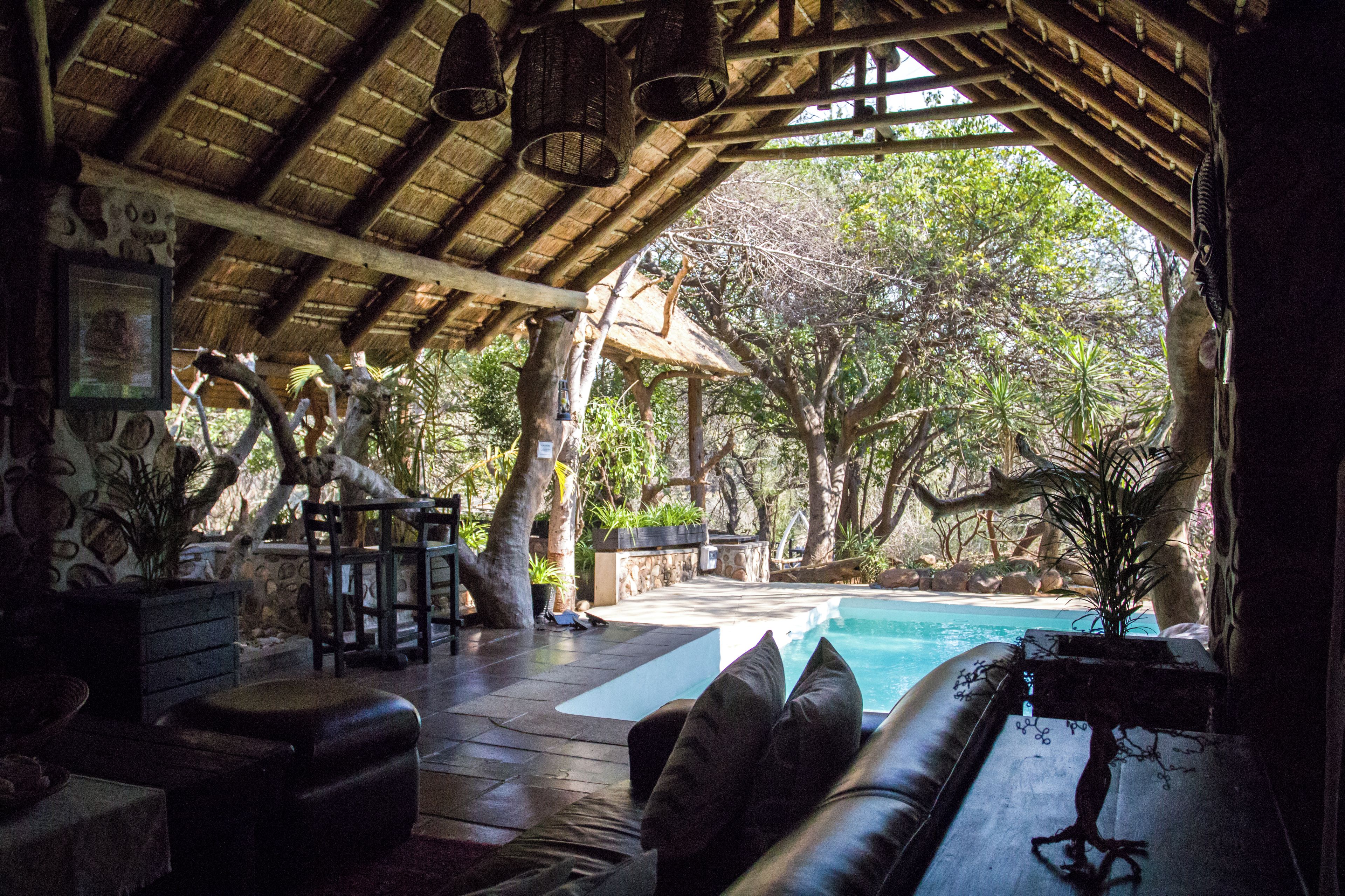 An indoor area with a pool, wooden furniture, and a thatched roof.