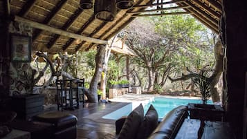 An indoor area with a pool, wooden furniture, and a thatched roof.
