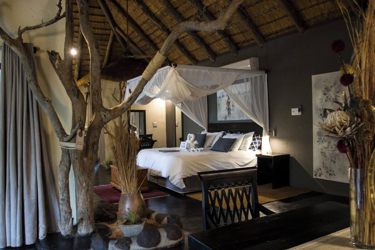 A bedroom with a canopy bed, a stone fireplace, and a large painting on the wall.