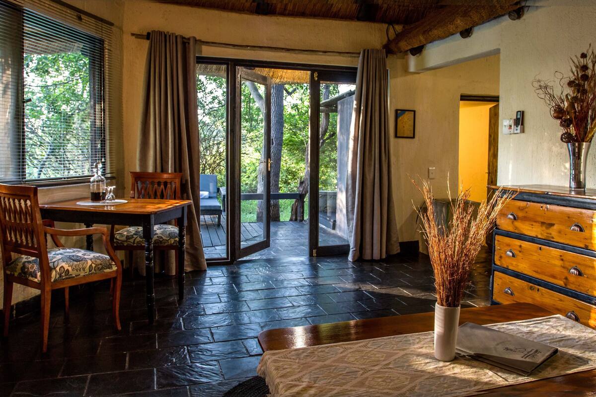 A room with a wooden dining table, chairs, a dresser, and a vase with dried plants.