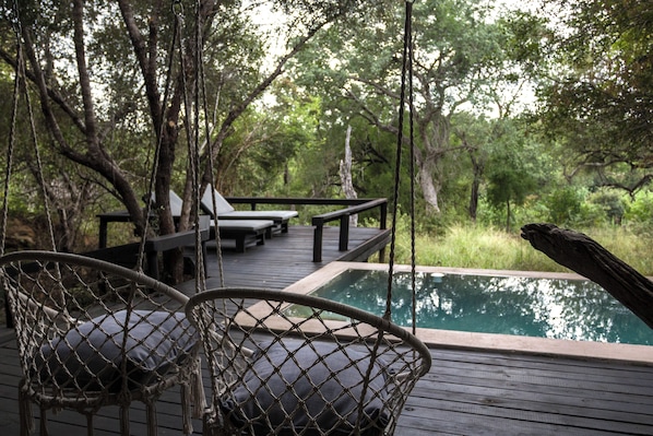 A wooden deck with a pool, surrounded by trees.