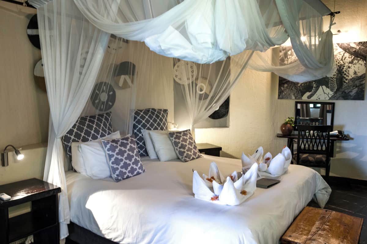 A bedroom with a canopy bed, multiple pillows, a bedside table, and a nightstand.