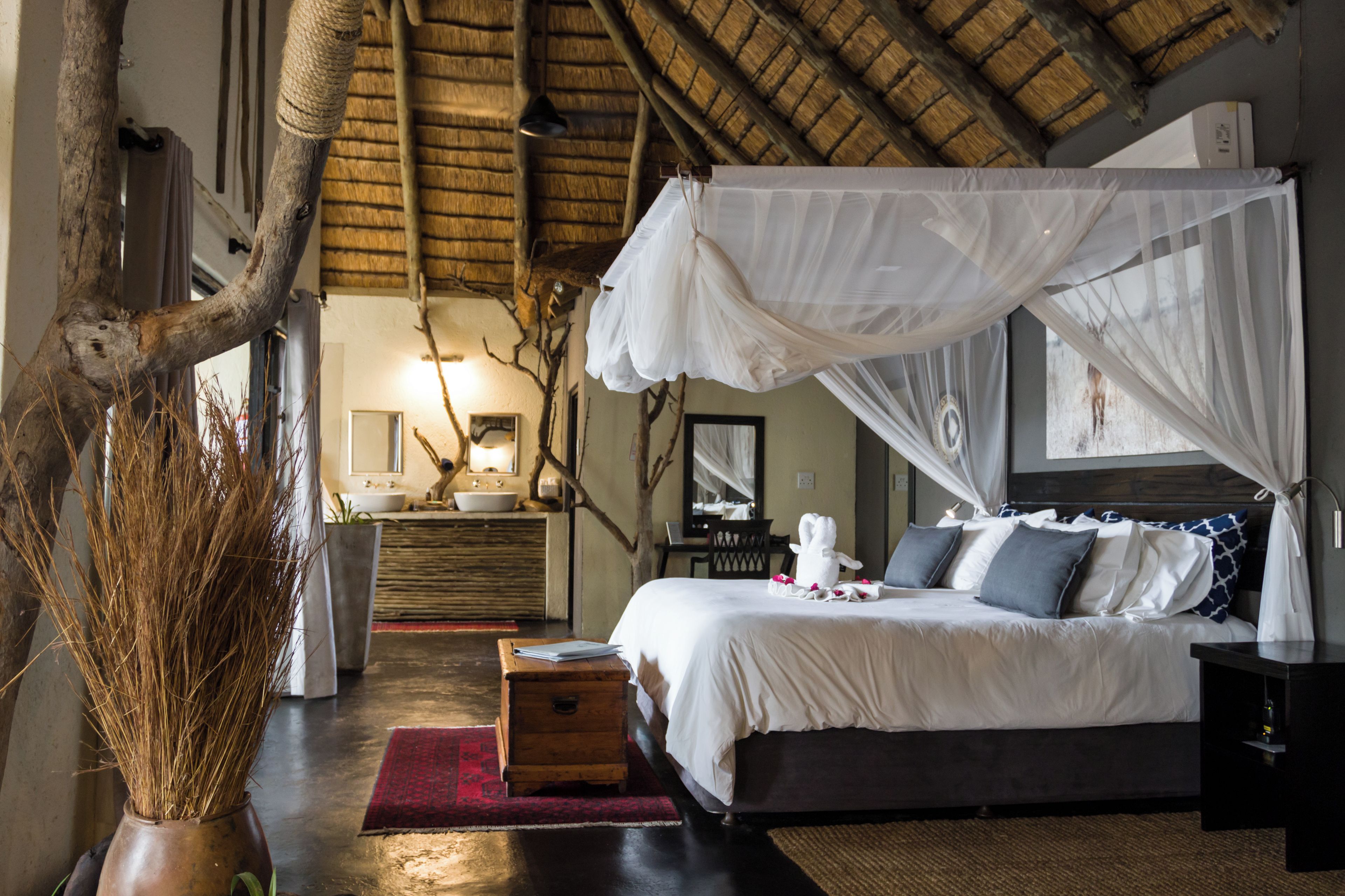 A bedroom with a canopy bed, a wooden dresser, a vanity with a mirror, and a large tree branch in the corner.