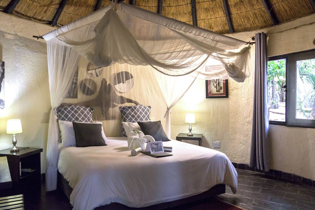 A bed with a canopy, bedside tables with lamps, and a window with curtains.