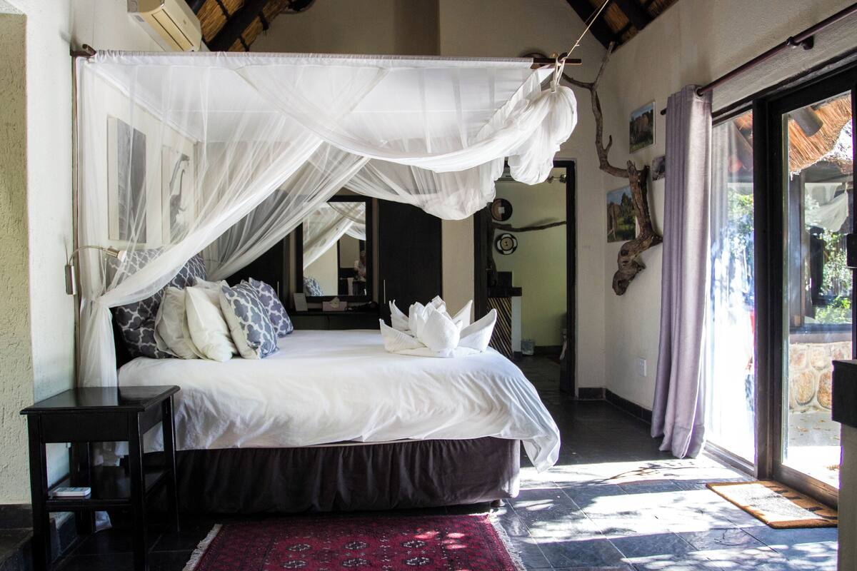 A bedroom with a large bed, a bedside table, a red rug, and a window with curtains.