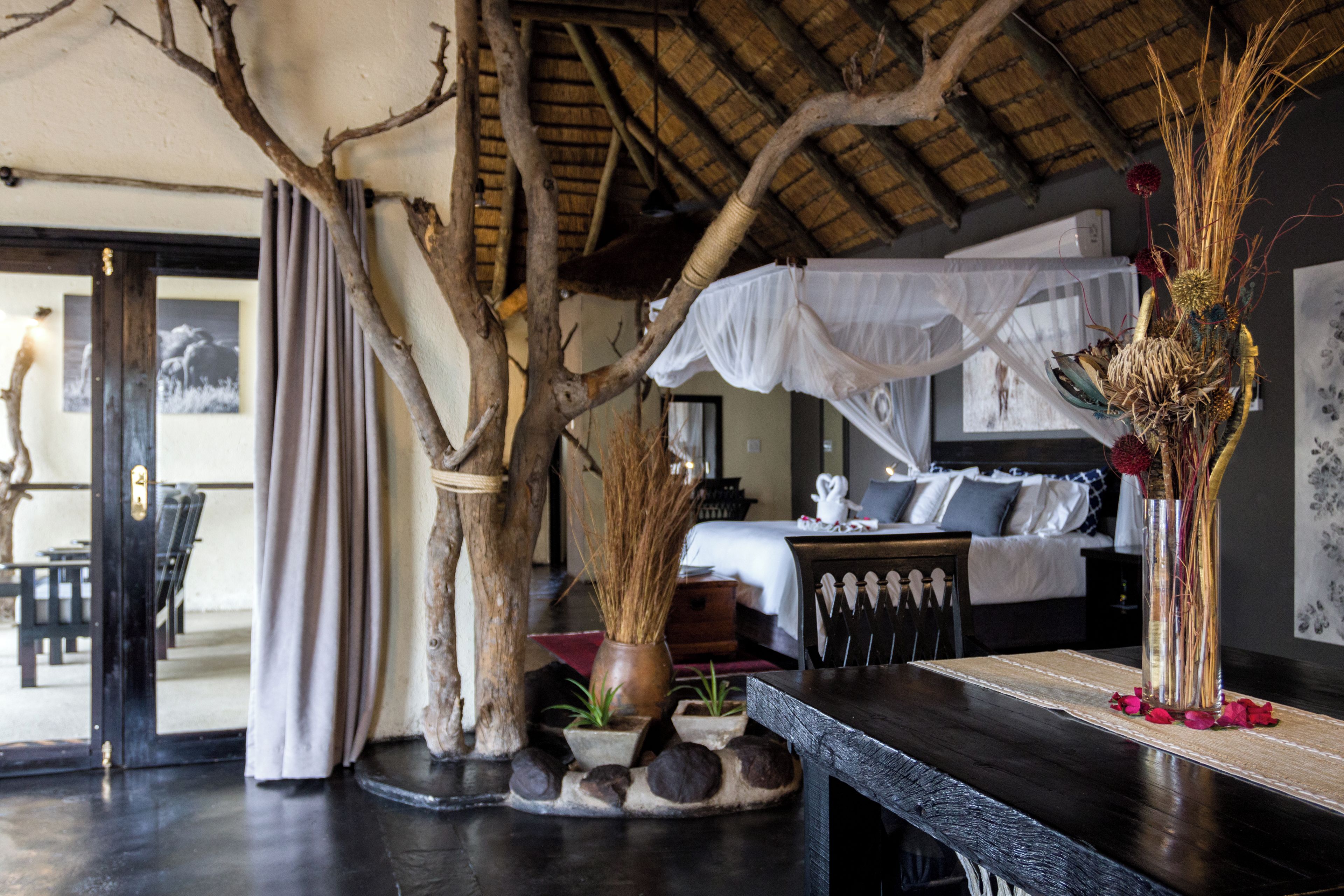 A room with a bed, a table, and a large tree trunk.