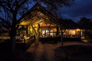 A rustic wooden structure with a thatched roof, surrounded by trees, and a dirt path leading to it. - Ezulwini Game Lodges (Hoedspruit)